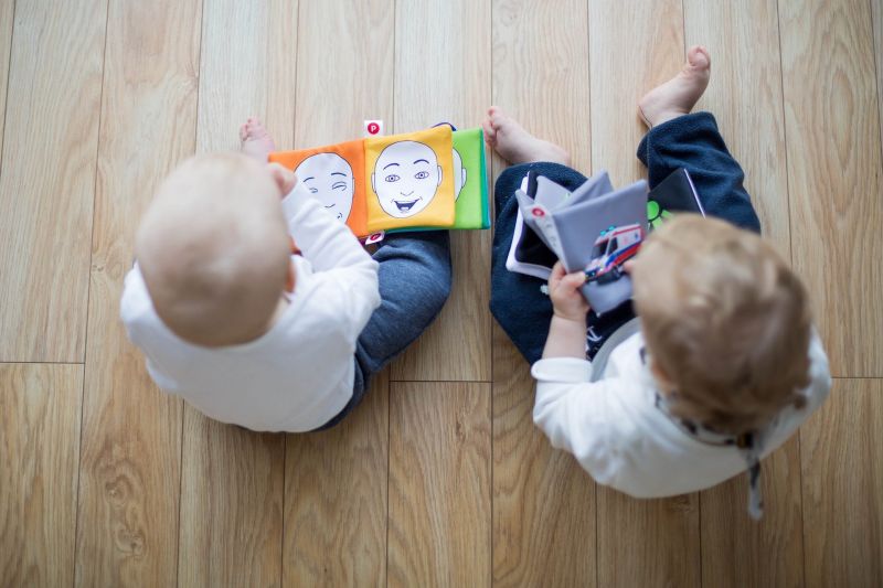 zwei Kleinkinder auf dem Boden, Stoffbilderbücher anschauend