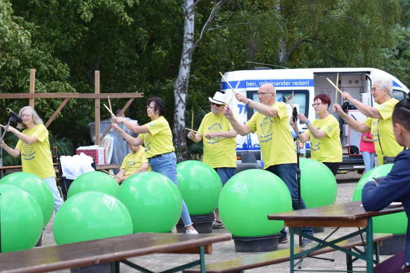 Gruppe von Personen in gelben T-Shirts trommelt auf grünen Gymnastikbällen