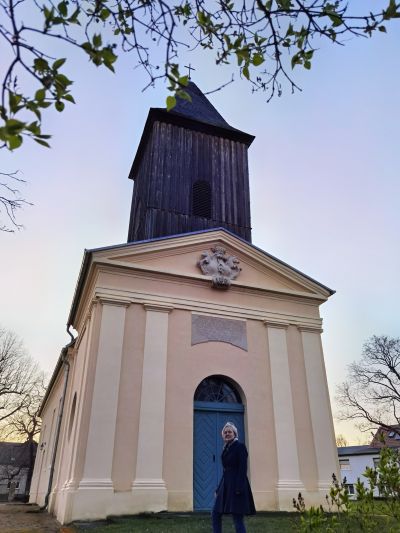 neoklassizisteiches Portal, hölzerner Glockenturm, Person im Vordergrund