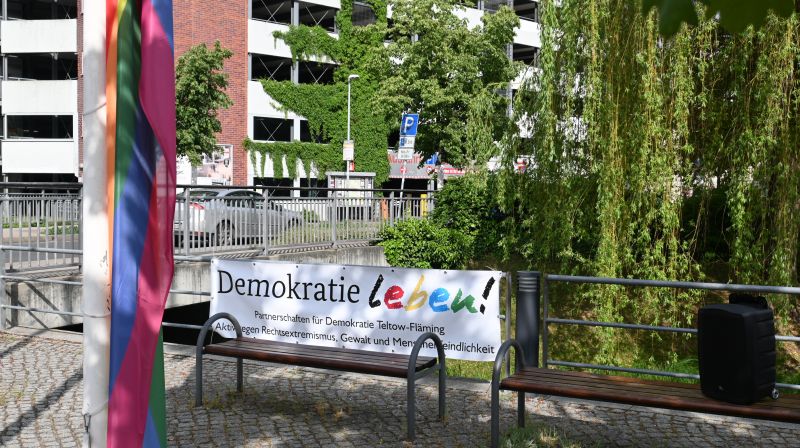 Banner mit Aufschrift Demokratie leben, davor Regenbogenflagge