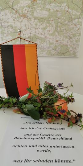 Text mit dem Gelöbnis, einer Deutschlandfahne und Blumen vor einer Landkarte des Landkreises Teltow-Fläming