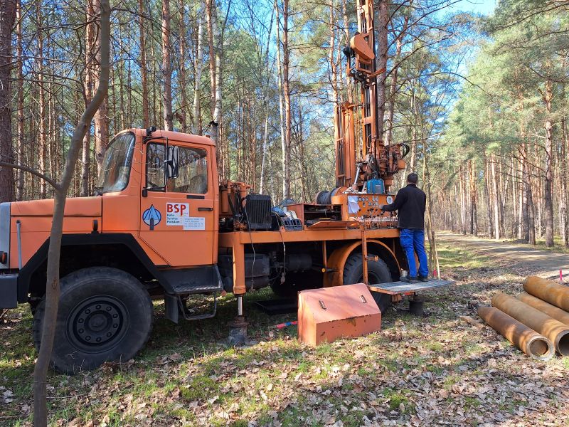 Mann bedient Baumaschine im Wald, im Vordergrund Rohre