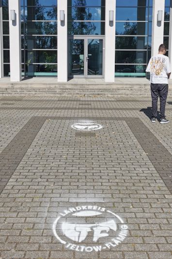 mit weißer Farbe auf den Boden gesprühte Logos des Landkreises als Wegweiser in den Festsaal